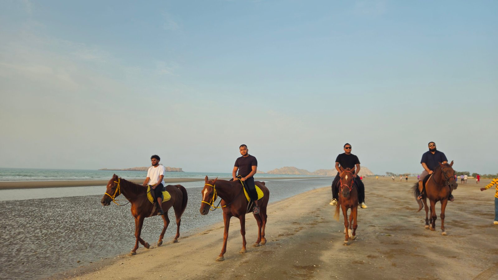 Riders on horseback along the sand at Al Sawadi Beach with the coastline behind