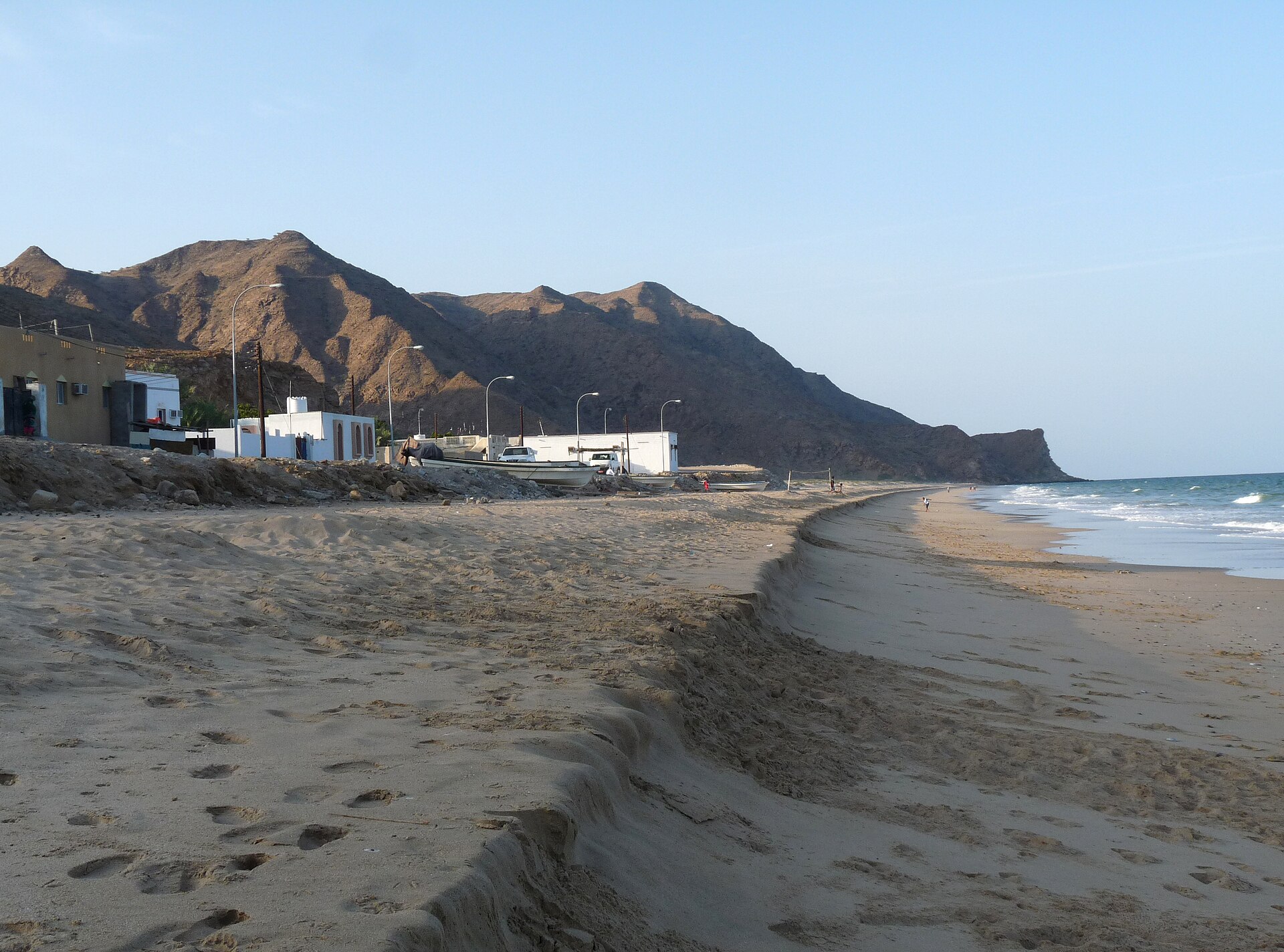 Fishing boats pulled up on the sand at As Sifah beach with the Hajar Mountains behind