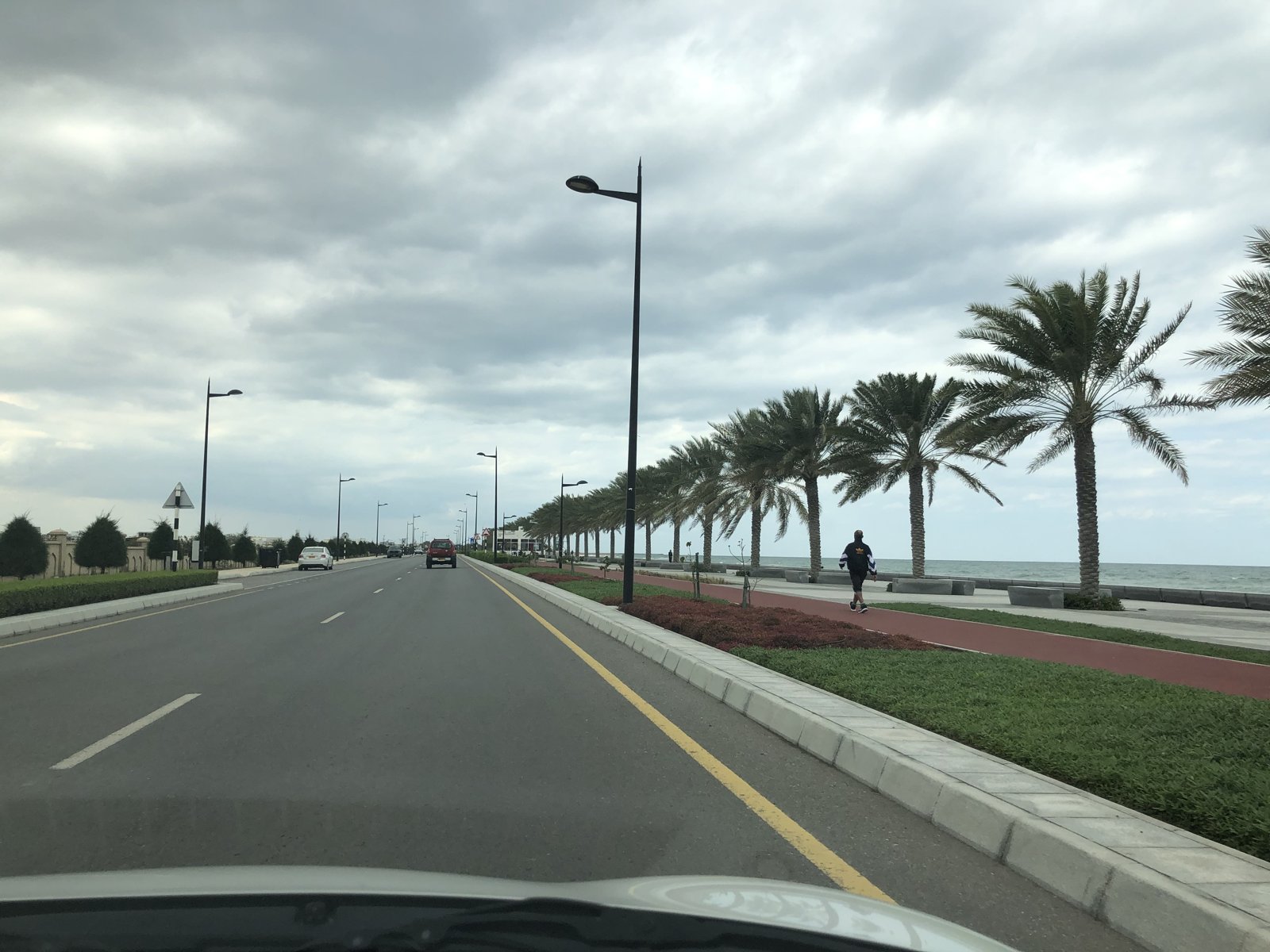 Seeb corniche road with its palm-lined jogging track and a runner beside the sea