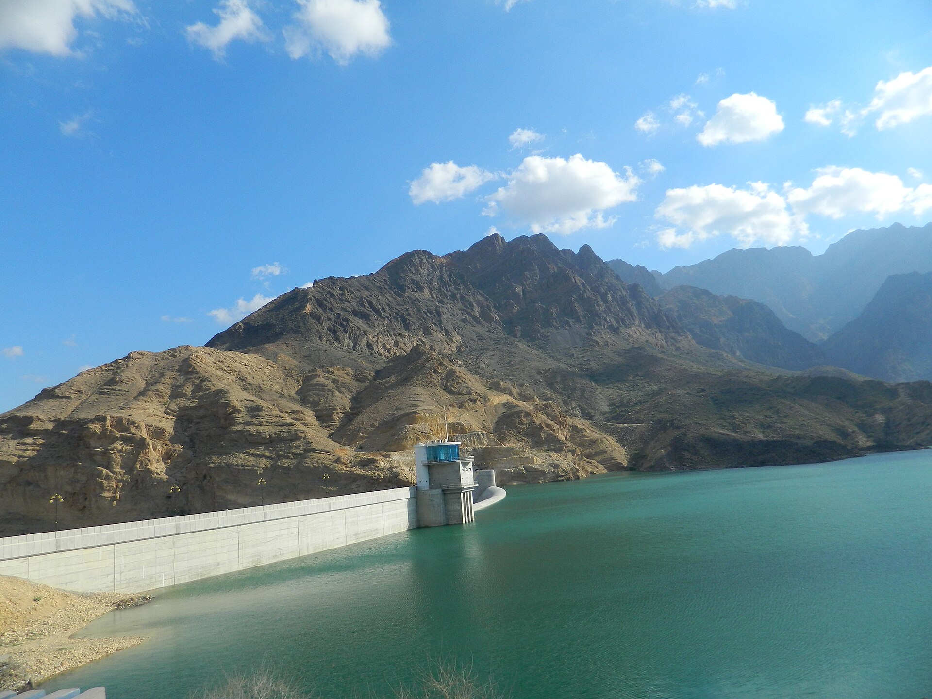 The turquoise reservoir of Wadi Dayqah Dam surrounded by the bare Hajar Mountains
